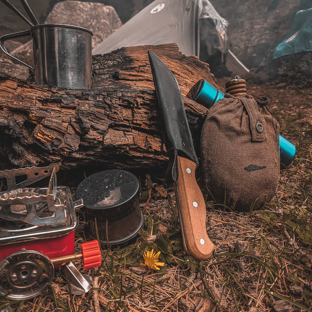 Essential camping gear including a knife, canteen, and cooking equipment on a campsite. Camping Accessories at Adventure Travel Gear.